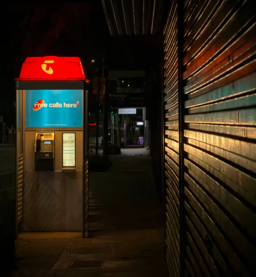 Telephone booth glowing red on a dark street at night